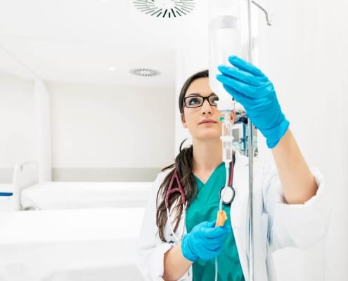 A healthcare professional from Boss Infusions, wearing blue gloves and a stethoscope, adjusts an IV drip in a bright, clean medical setting—delivering expert IV Infusion Therapy Brisbane can trust.