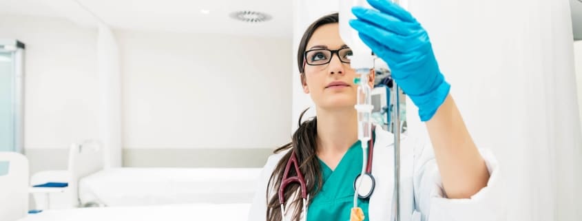A healthcare professional from Boss Infusions, wearing blue gloves and a stethoscope, adjusts an IV drip in a bright, clean medical setting—delivering expert IV Infusion Therapy Brisbane can trust.