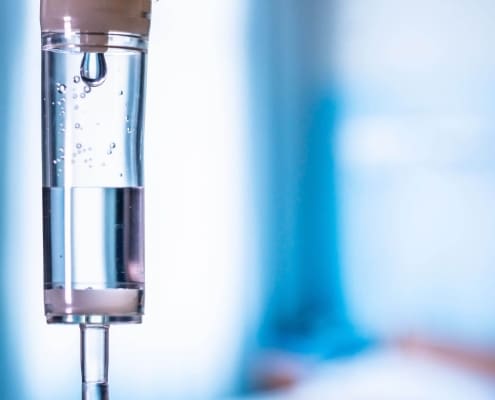 Close-up of an intravenous (IV) drip chamber with clear fluid and air bubbles, set against a blurred blue and white background, highlighting the professional care offered by Boss Infusions IV Infusion Therapy Brisbane.