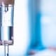 Close-up of an intravenous (IV) drip chamber with clear fluid and air bubbles, set against a blurred blue and white background, highlighting the professional care offered by Boss Infusions IV Infusion Therapy Brisbane.