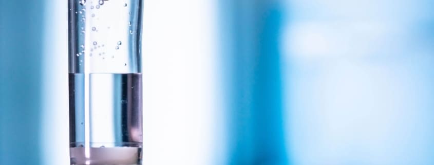 Close-up of an intravenous (IV) drip chamber with clear fluid and air bubbles, set against a blurred blue and white background, highlighting the professional care offered by Boss Infusions IV Infusion Therapy Brisbane.