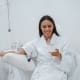 A woman in a white robe sits in a chair at Boss Infusions, receiving IV Infusion Therapy Brisbane while smiling and holding a glass of wine. The bright, clinical setting suggests a relaxing spa or wellness clinic experience.